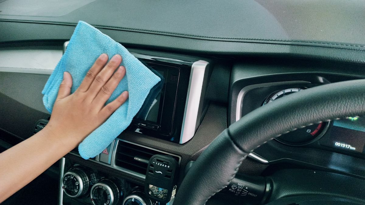 Hand wiping down a car dashboard with a microfiber cloth